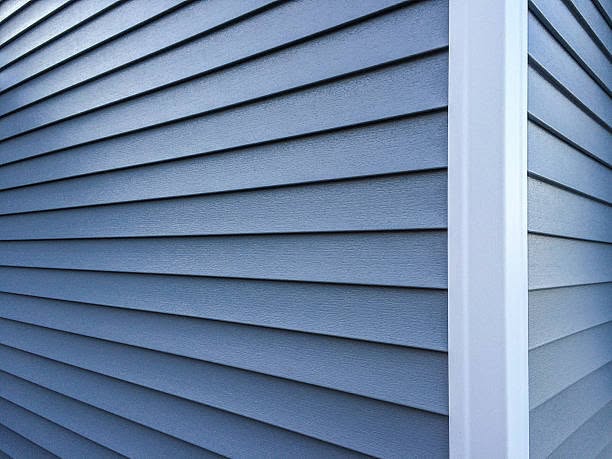 Close-up view of textured blue-gray horizontal vinyl lap siding joining at a white outside corner post.