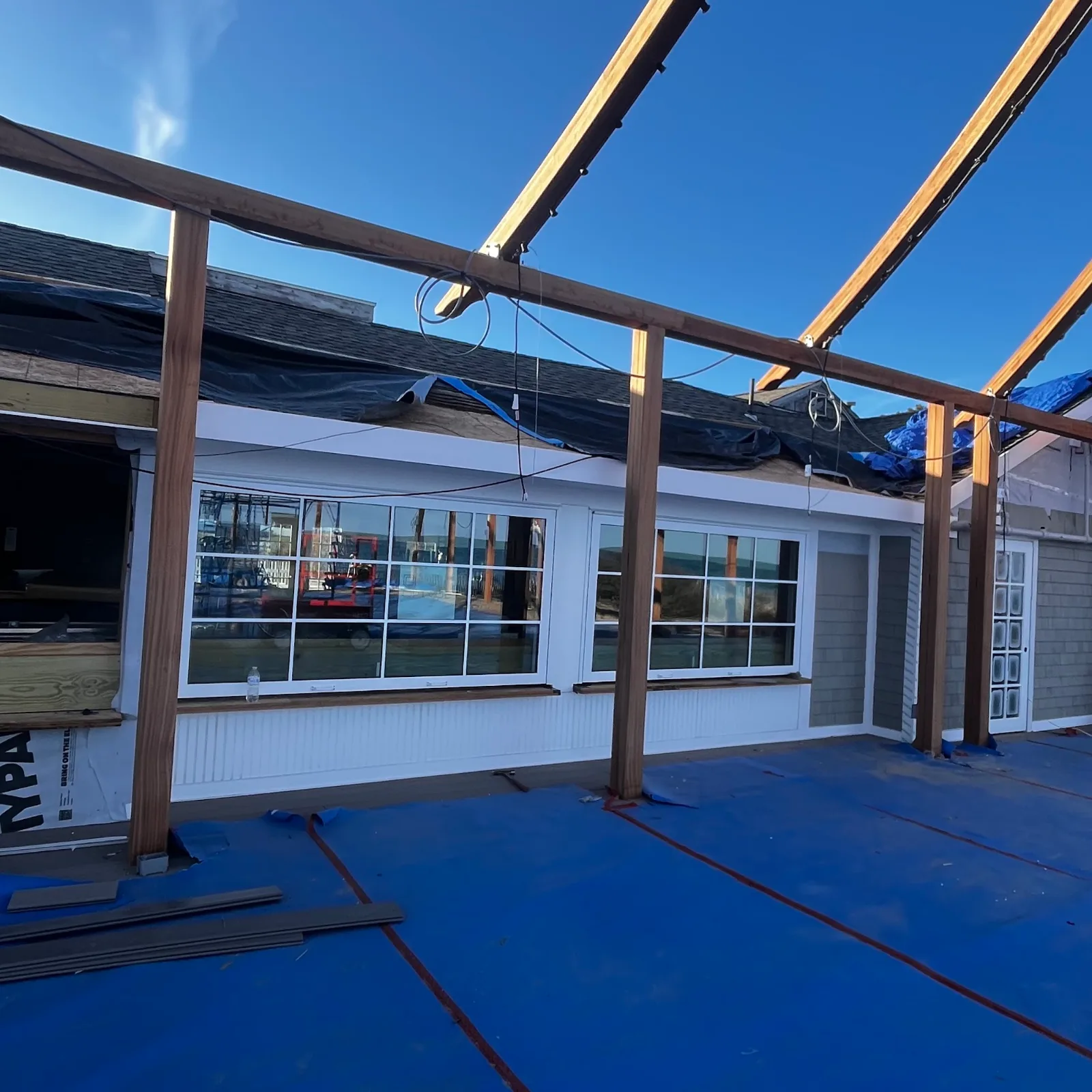 Commercial roofline covered with underlayment and tarps during roofing work, with new timber framing overhead