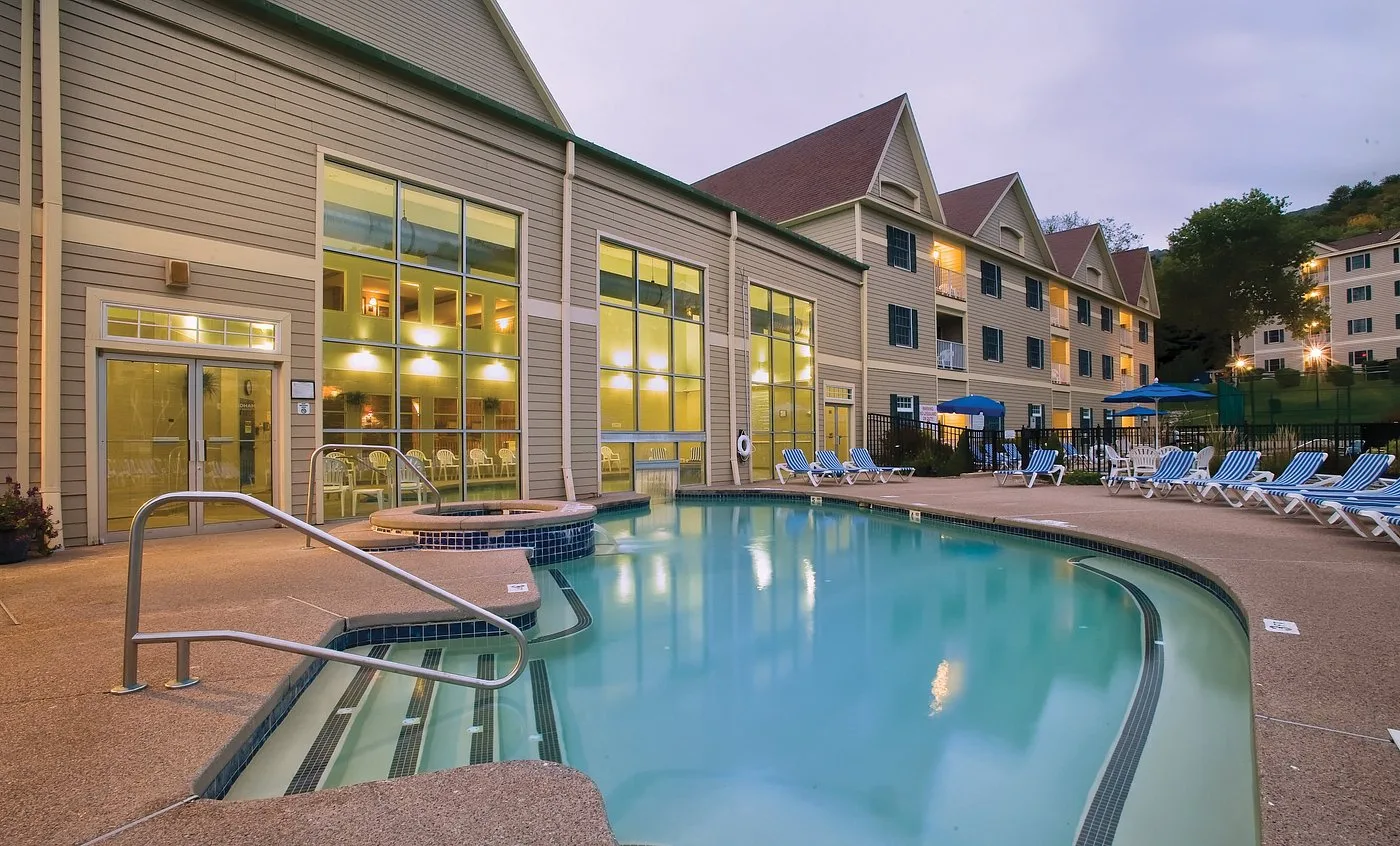 Multi-story commercial building with beige siding and gabled rooflines beside an outdoor pool